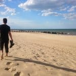 A man walking barefoot on a sandy beach, on the East coast of England.