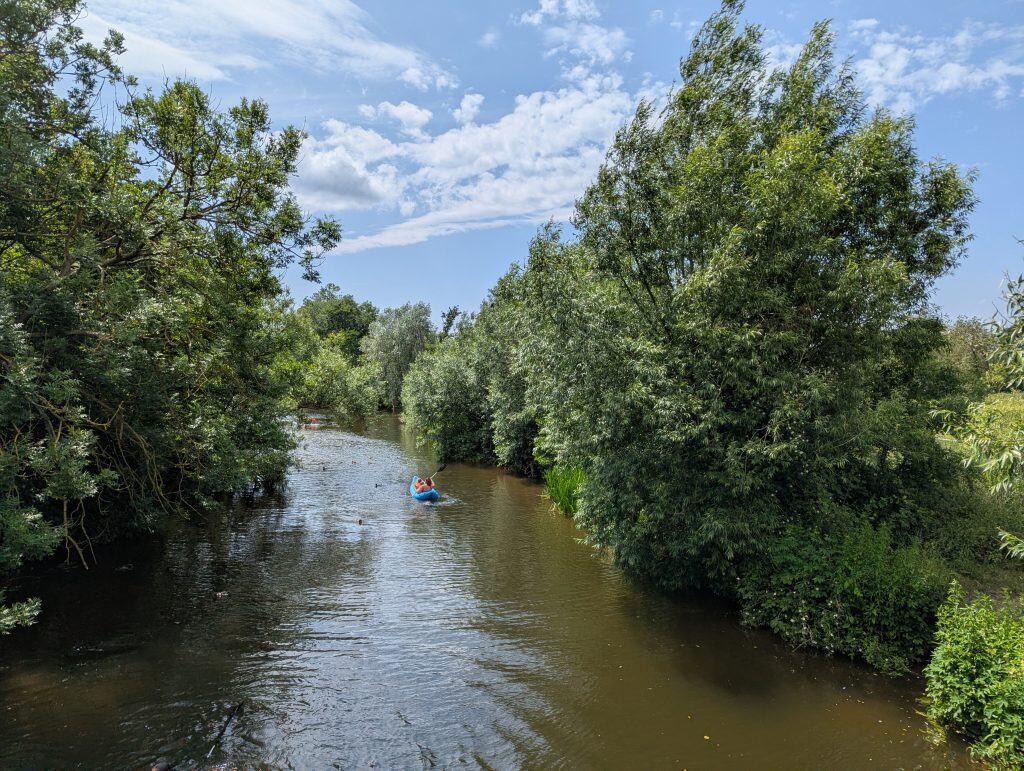 A person kayaking in Dedham on a river on a sunny day.