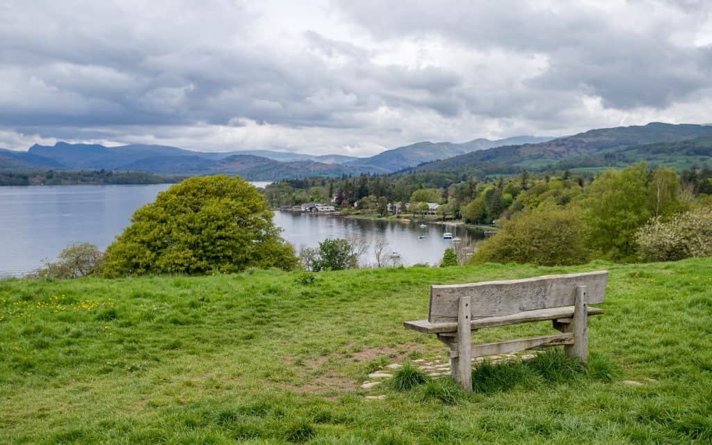 A wooden bench with a lake and hills at back.