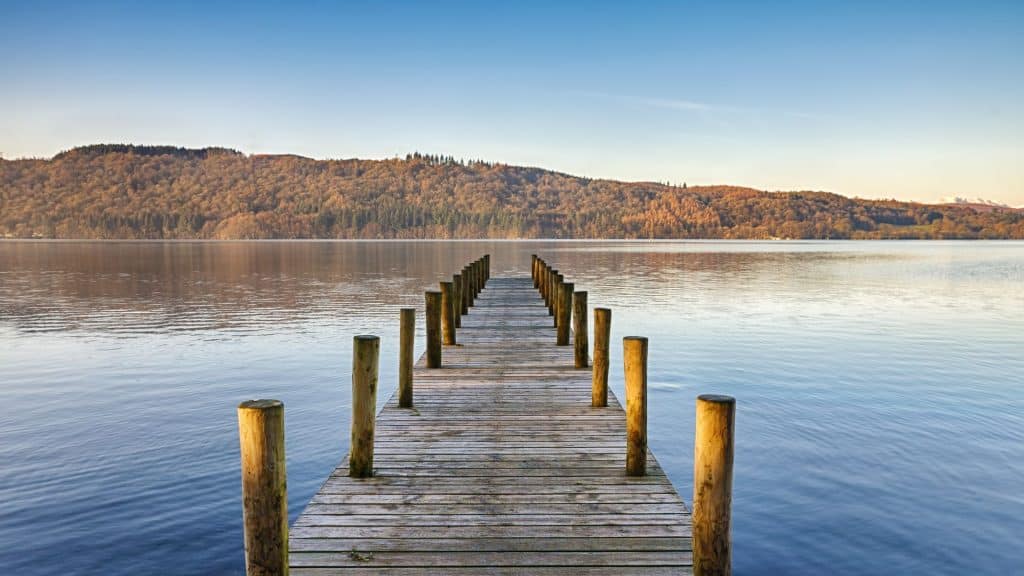 A view at a wooden pier/jetty and a lake with a hill and forest.