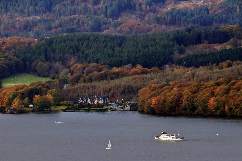A boat on the Windermere Lake in autumn with colourful trees.