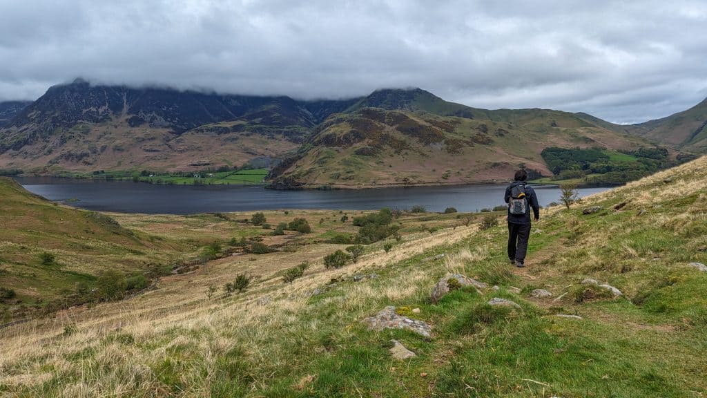 A man walking near Buttermere Lake on a cloudy day.