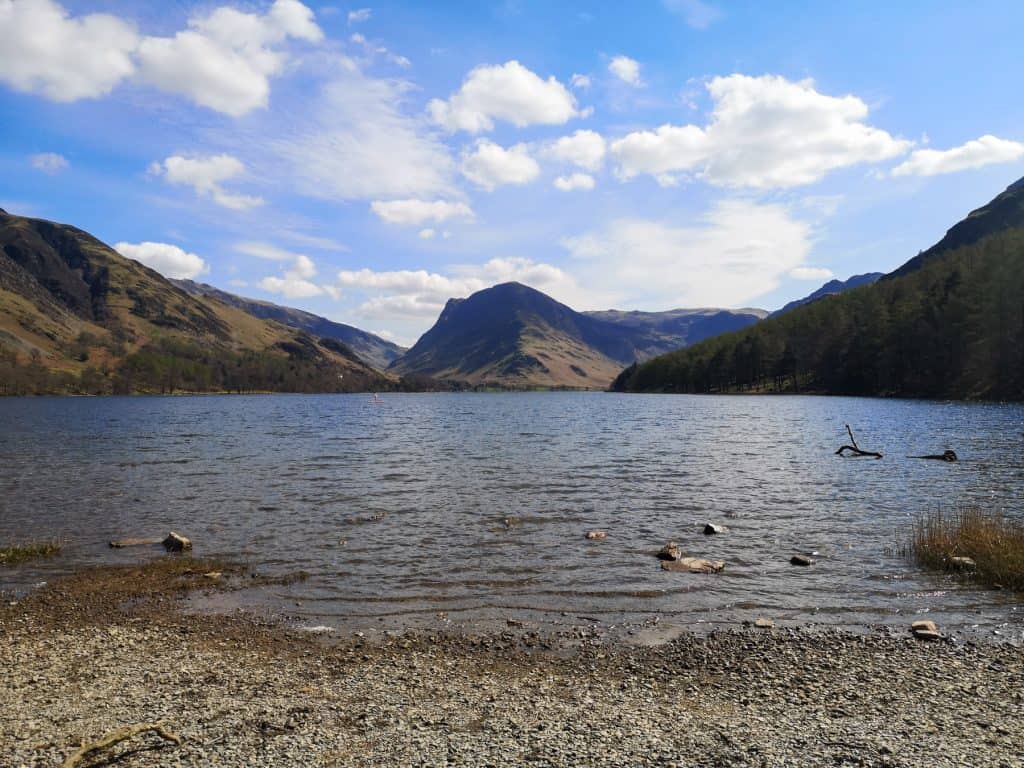 Buttermere lake on a sunny day with a person paddleboarding.