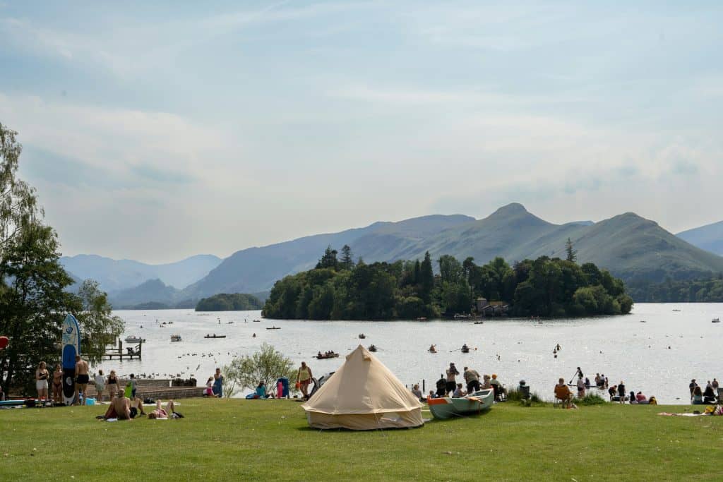 People resting on the shore of a lake in the Lake District in summer.