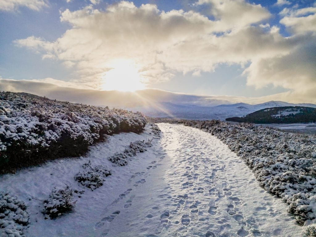 View at a path covered in snow on a sunny day in Scotland in winter with mountain views.