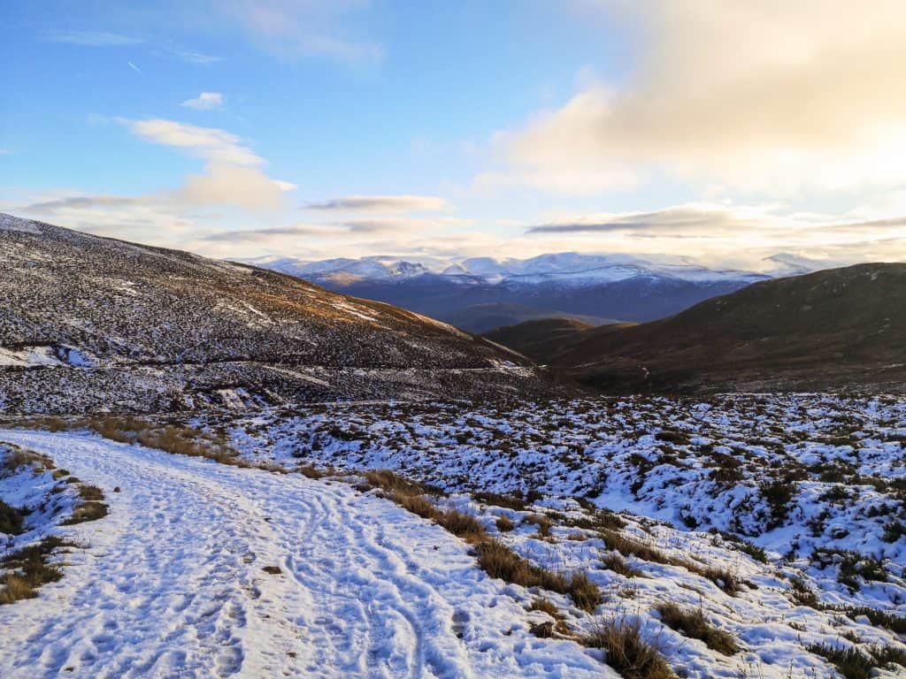 View at a path covered with snow on a sunny day in Scotland with mountain views. airngorm is one of the best places to visit in UK in February. 
