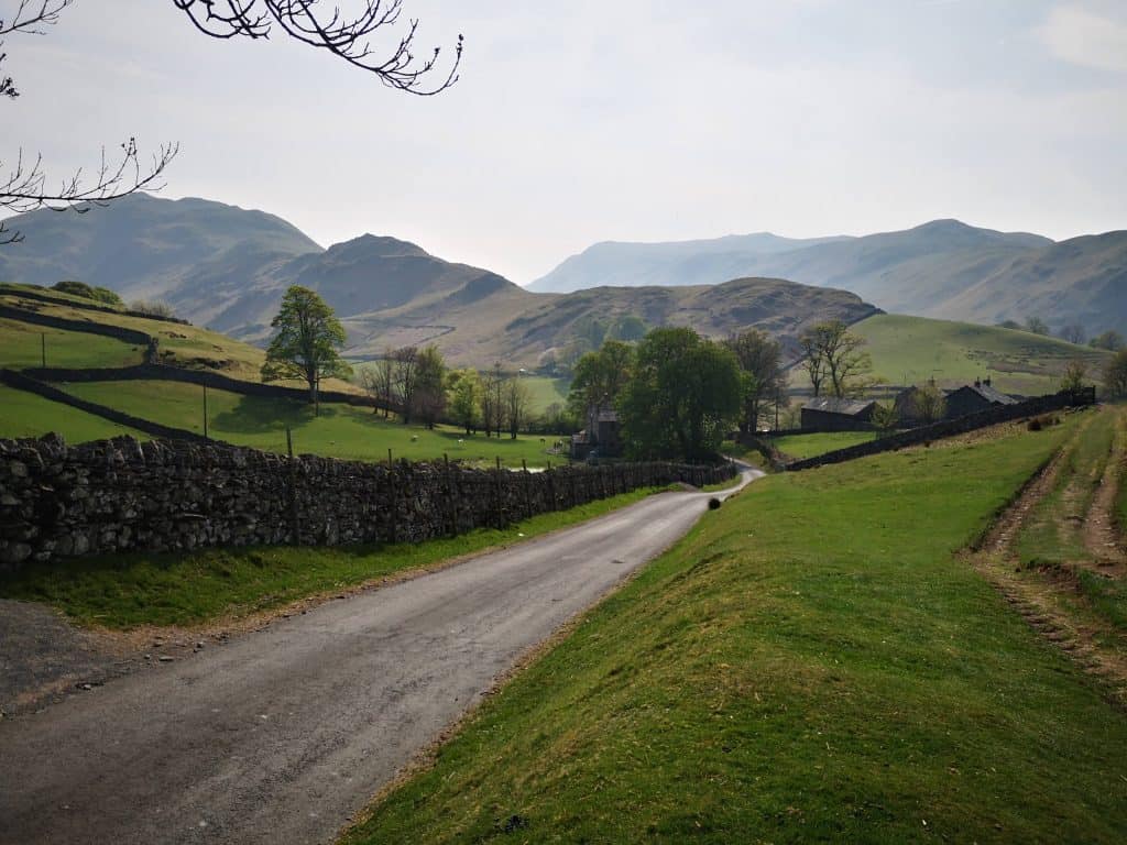 Small cottages near a tiny road in Lake District with hills at back.