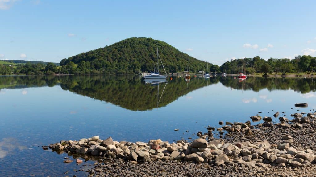 A lake at the Lake District with boats and a hill covered in forest.
