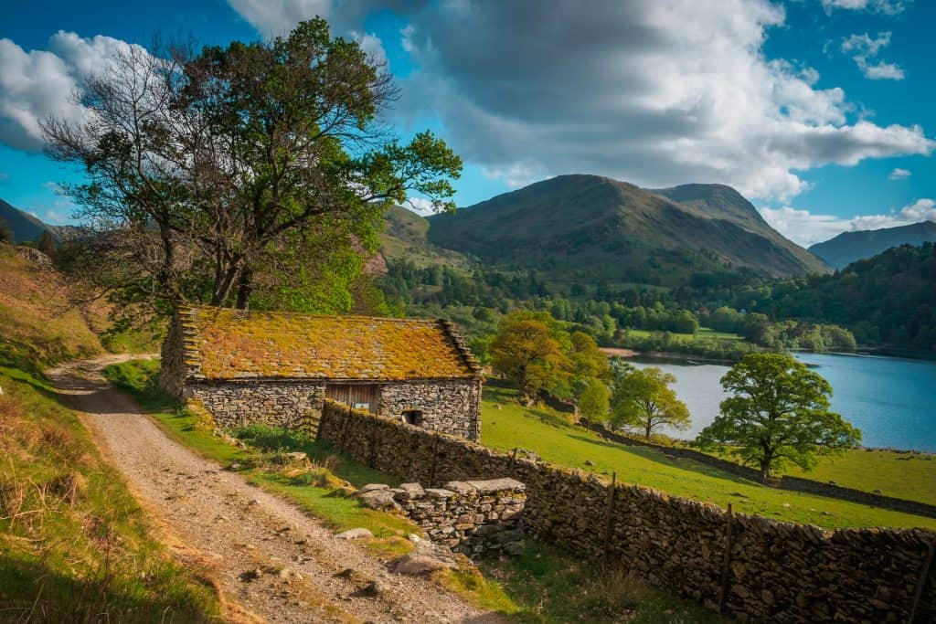 Small old stone cottage with a lake, trees and hills at back, picturesque views during Ullswater walks.