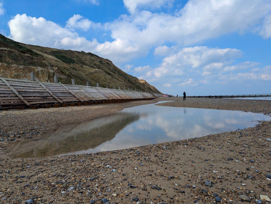 Trimingham Beach in Norfolk - view at the cliffs, person taking photos and a tide pool.