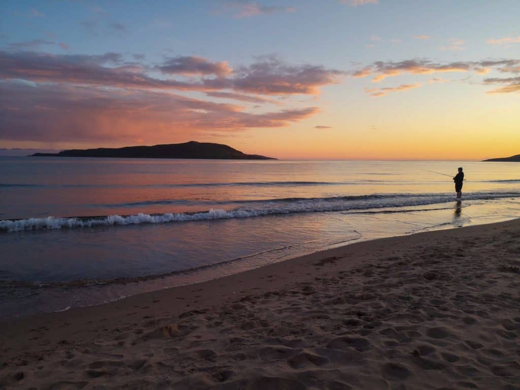Beach on the NC500 route during a sunset with a man fishing.