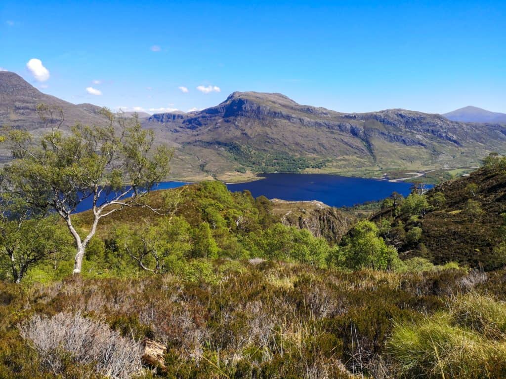 Scotland Itinerary - Hiking on the NC500 route, views showing a lake, trees and mountains on a sunny day.