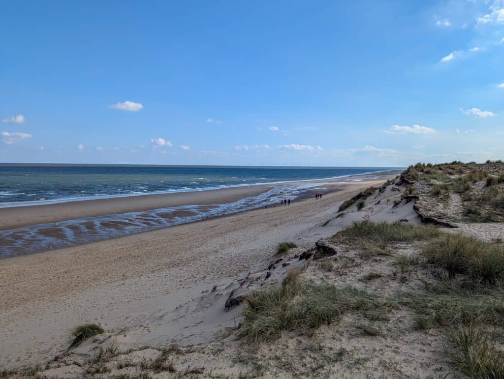 View at the sea and people walking on the sandy Winterton Beach on a sunny day.