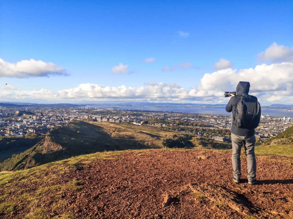 A photograph taking a photo of the Salisbury Crags and the city from one of the pathways to the Arthur Seat in Edinburgh.