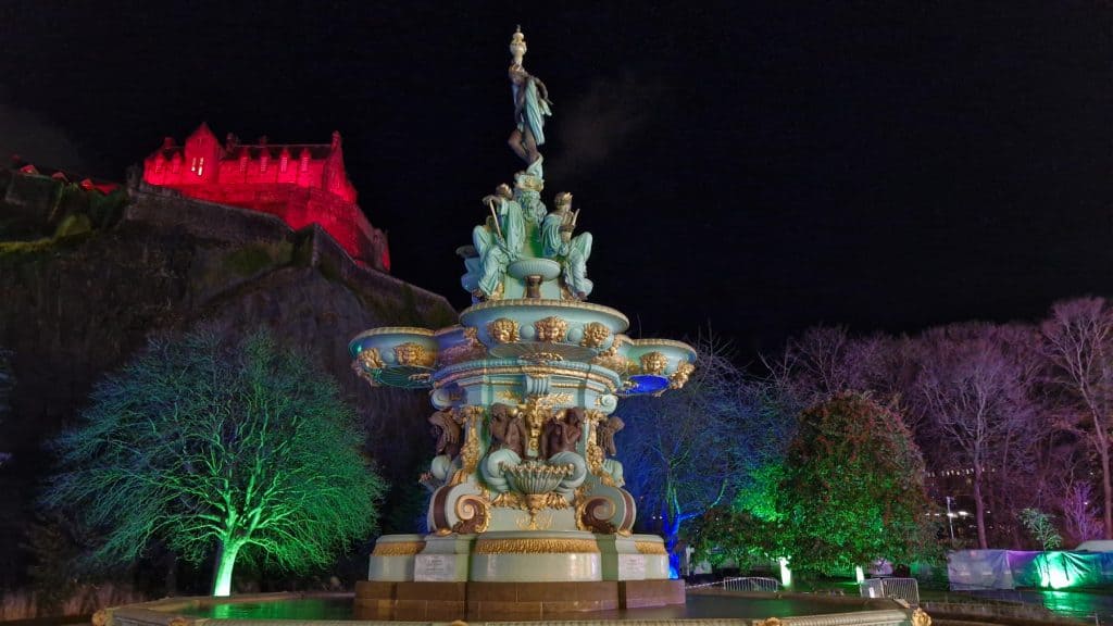 Illuminated Edinburgh Princes Street Gardens with a fountain during Christmas Market.