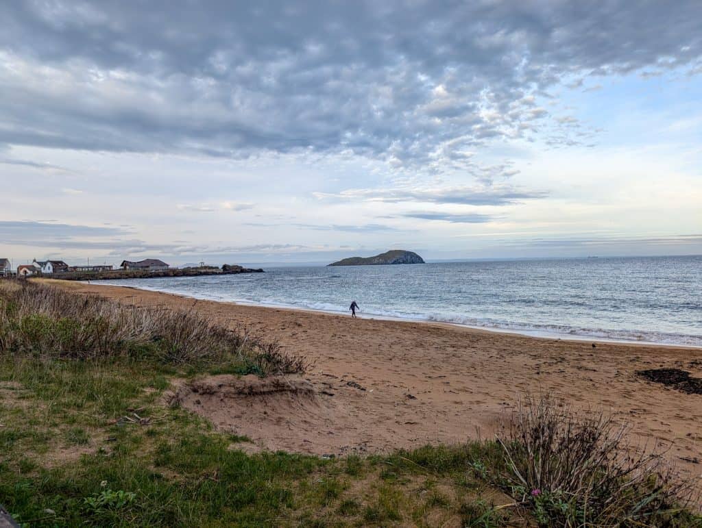 A person walking on a beach in North Berwick with cliffs at distance, one of the best things to do in North Berwick. This beach is among the best beaches near Edinburgh.