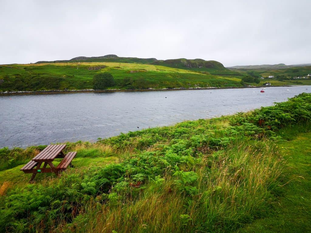 Viewpoint - Amar river with boats, cottages and a bench with green hills at distance on a cloudy day.