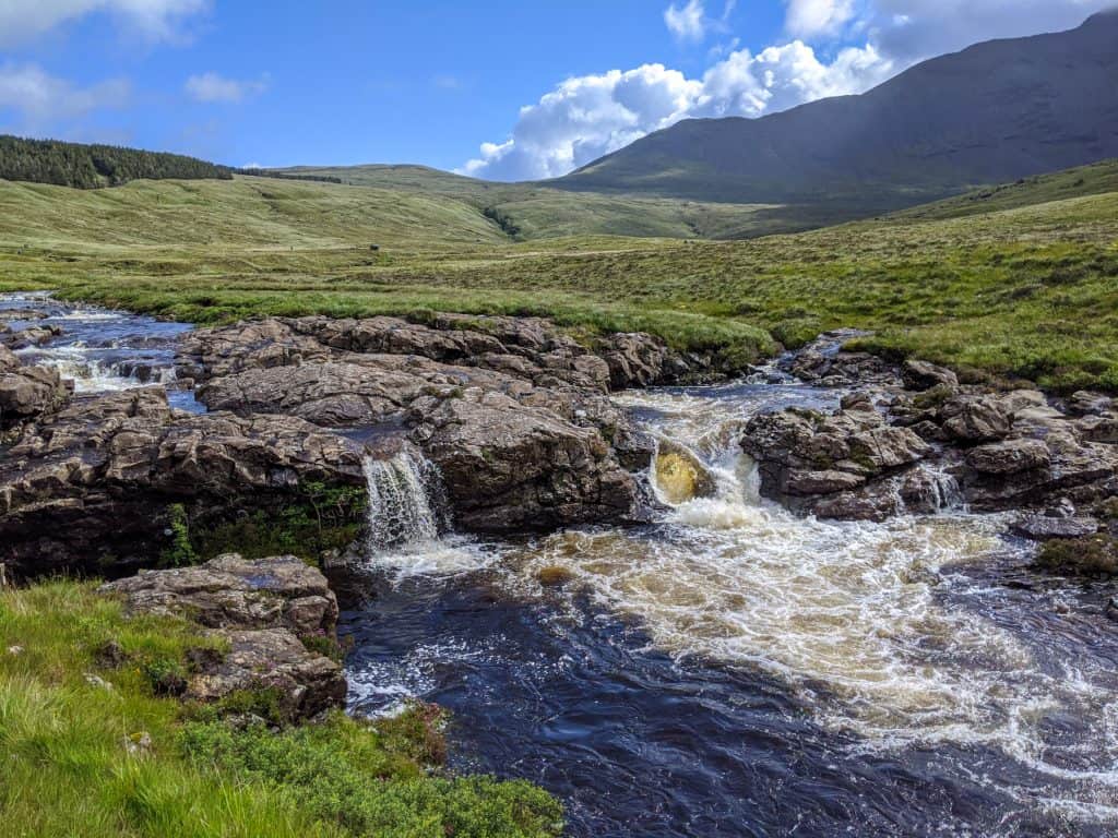A river with tiny waterfalls and pools on a sunny day on the Isle of Skye. Fairy Pools are a must for every Isle of Skye Guide.