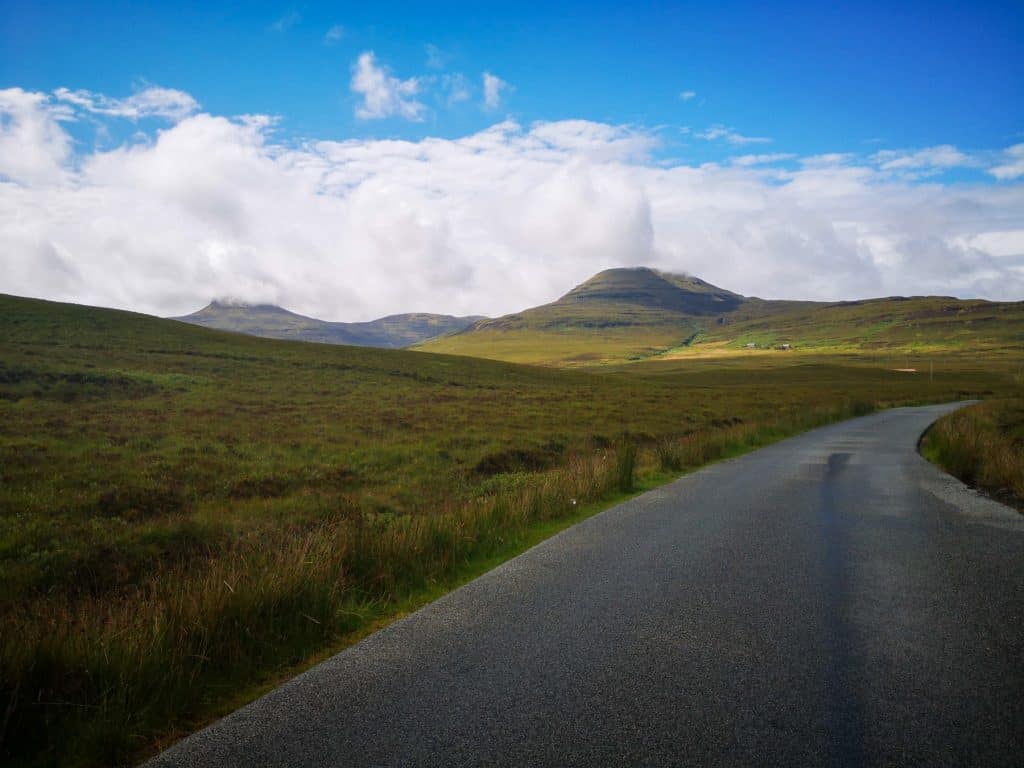 A road with hills at back on a sunny day on the Isle of Skye.