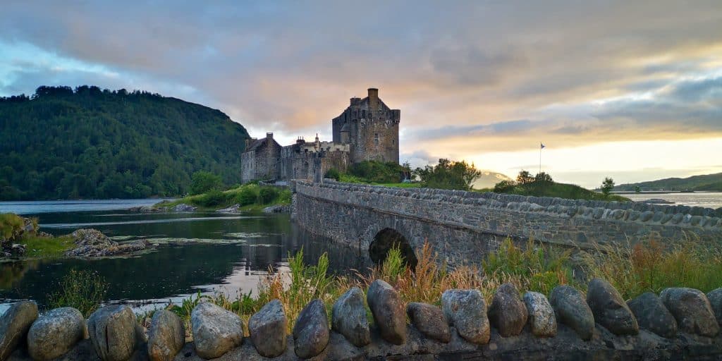 Old medieval castle with bridge over a lake during sunset.
