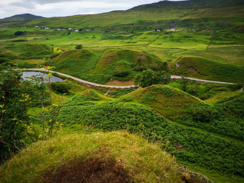 Fairy Glen with hills and views on a stunning greenery, small lake and cottages in distance.