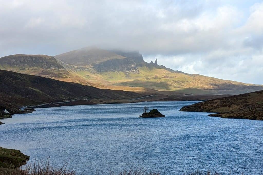 View at the waters of Loch Fada with small island with a tree and Old Man of Storr at back.