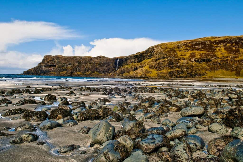 Beach with rocks, sea and rock formations with a waterfall on a sunny day.