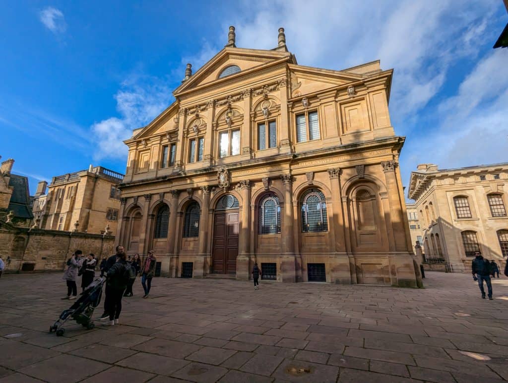 Sheldonian Theatre building on a sunny day with people standing around it.