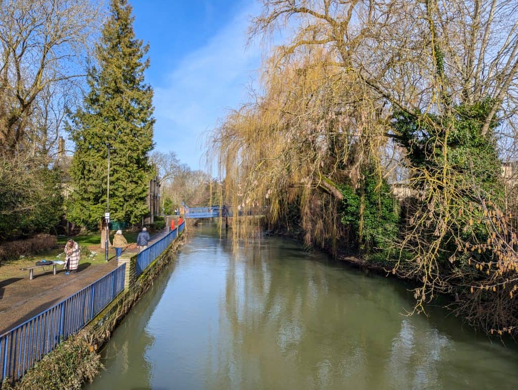 People walking next to the river on a sunny day in early spring.