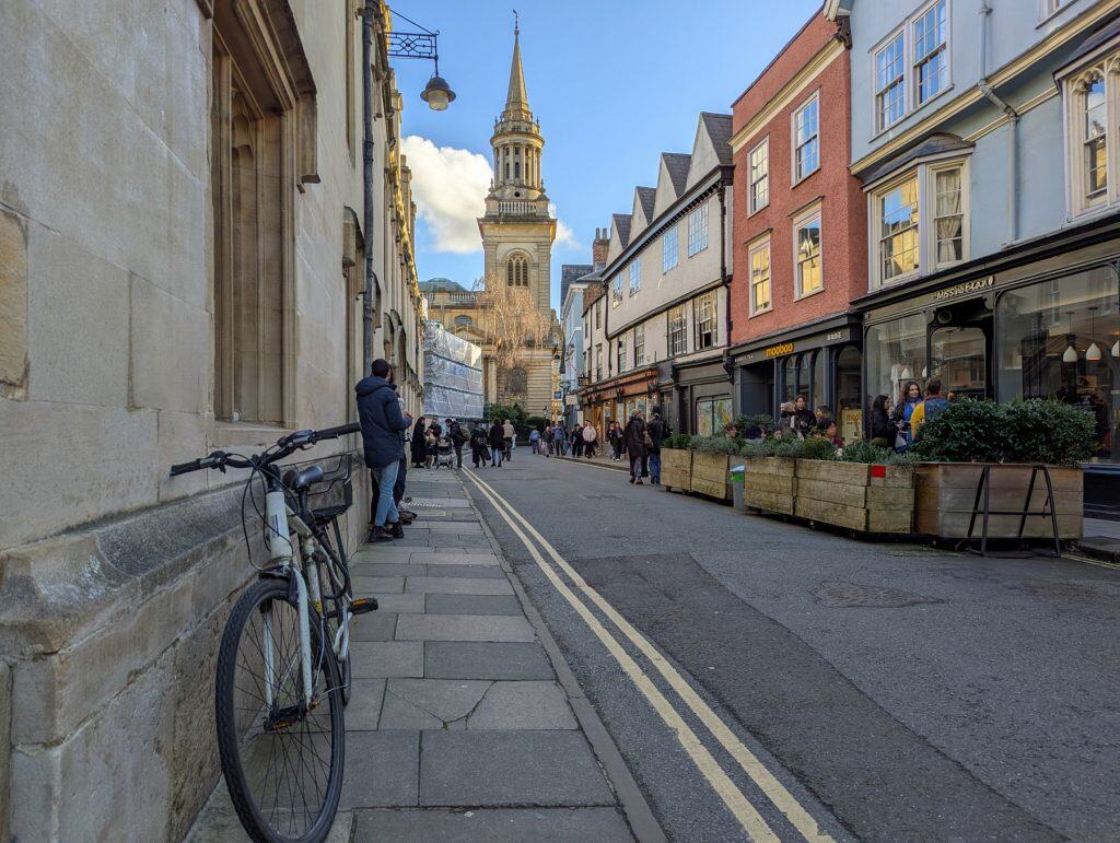 Busy street in Oxford with people on a sunny day with a church at back.