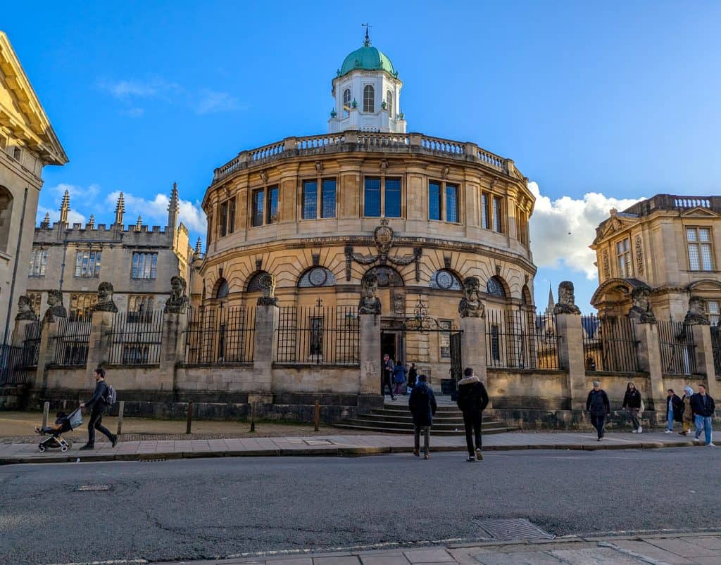 A building of the Sheldonian Theatre with people around it.