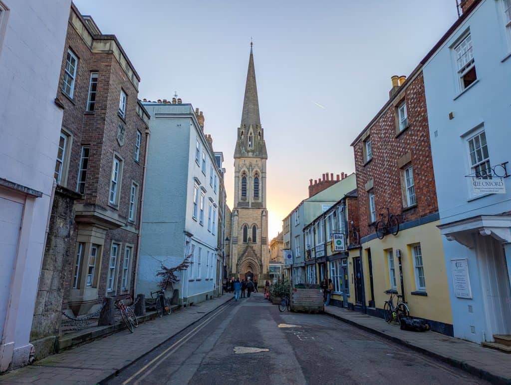 A mediaeval street in Oxford with a church at back during sunset; walking is an essential part of a perfect day trip to Oxford.