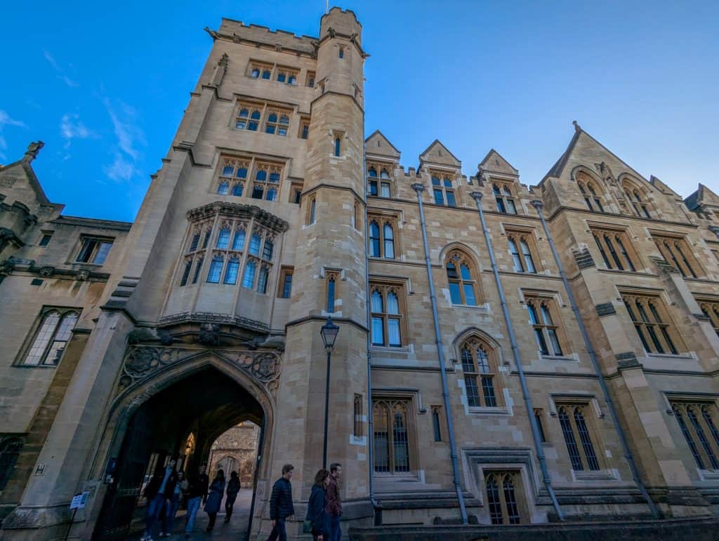 Mediaeval buildings and entrance gate of the New College in Oxford with people.
