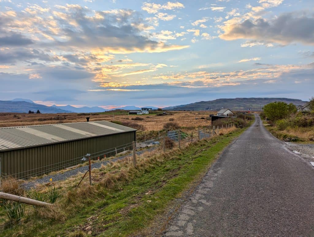 Sunrise on the Isle of Mull with a single track road, cottages and mountains at back.
