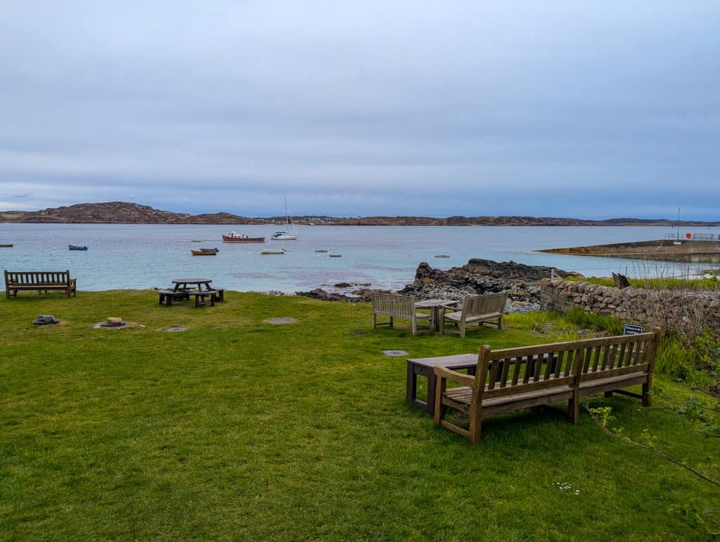 Benches and tables near a beach on the Isle of Iona with boats at back.