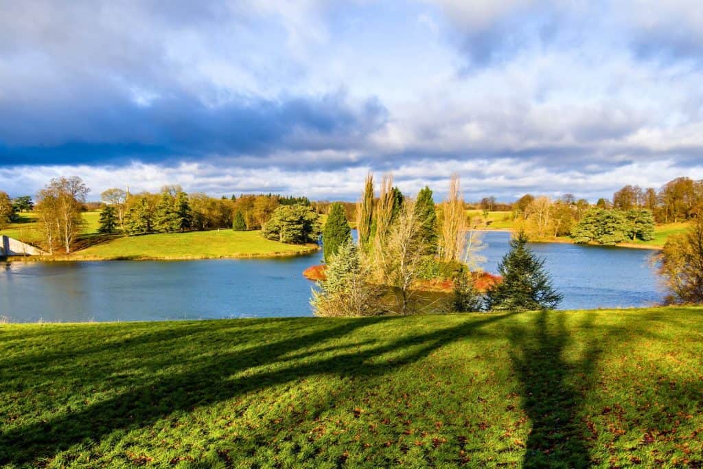 Gardens of Blenheim Palace in autumn on a sunny day with river and trees.