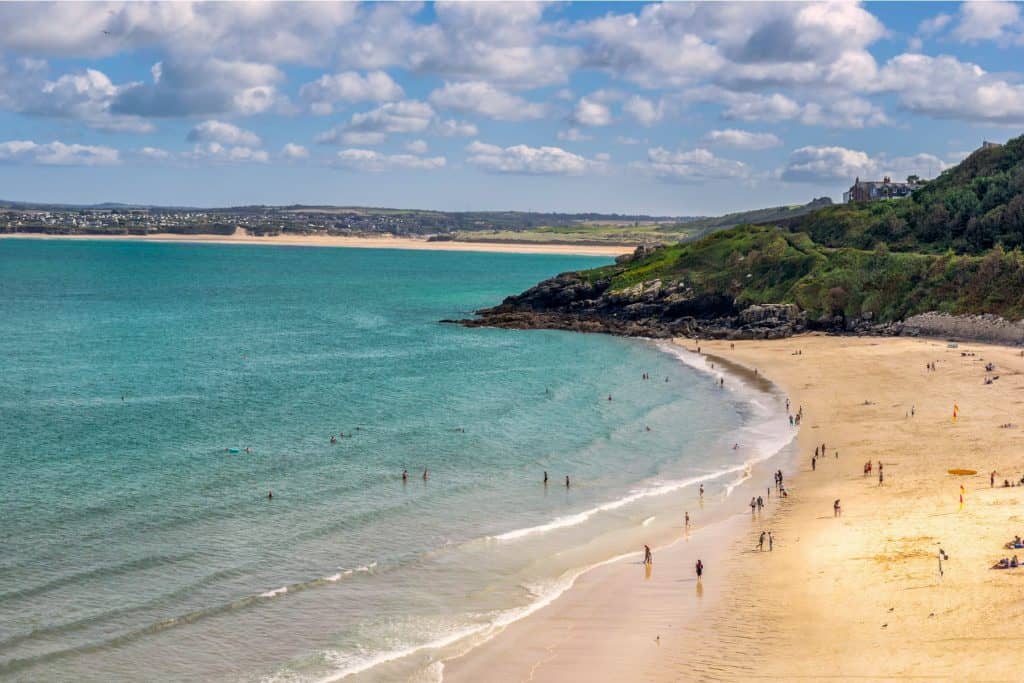 Sandy beach with sea and cliffs with people walking.