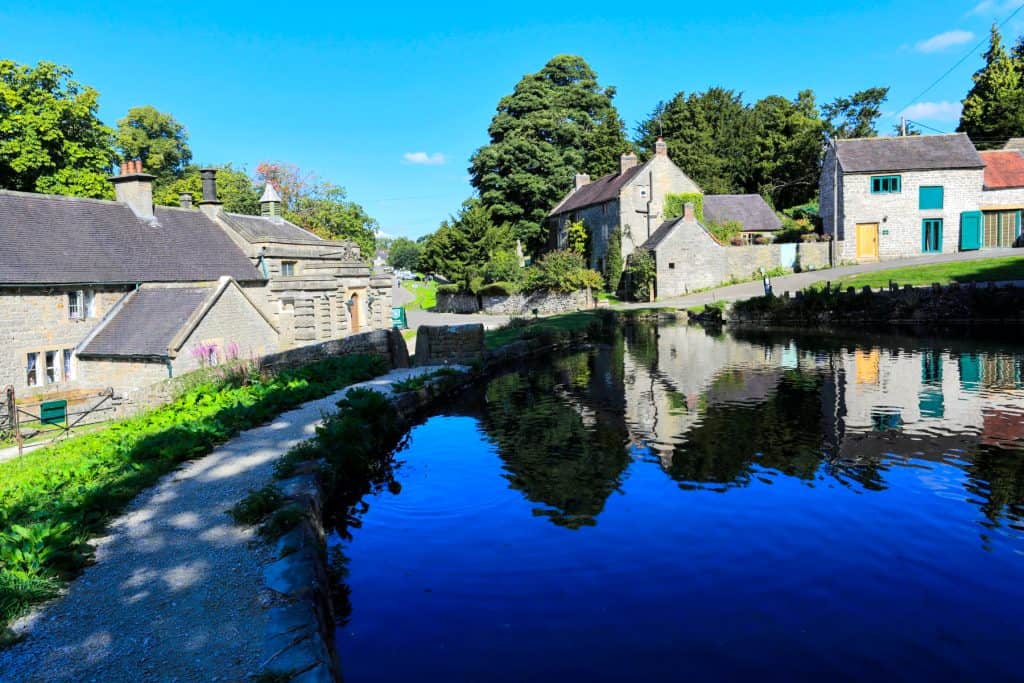 A small pond with a street with old stone cottages.