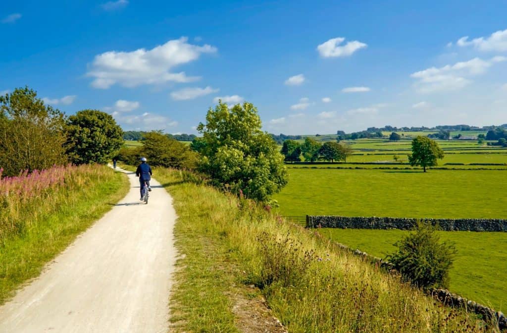 Cyclists on a trail in Peak District with meadows views.