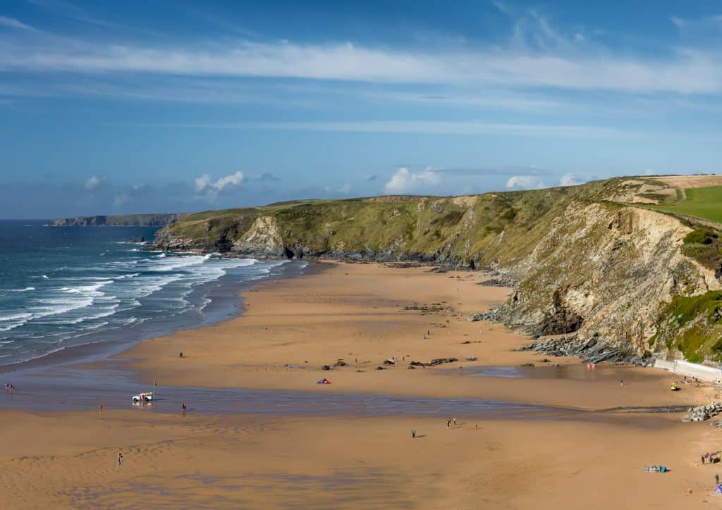 Long sandy beach with sea and massive cliffs.