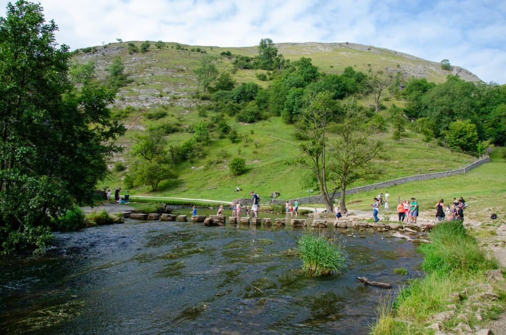 Dovedale Stepping Stones - a river with people going through the river with hills at back.