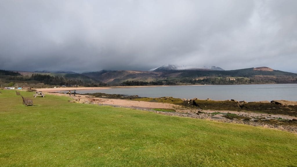 Sandy beach with snowy mountains at back on a cloudy day.