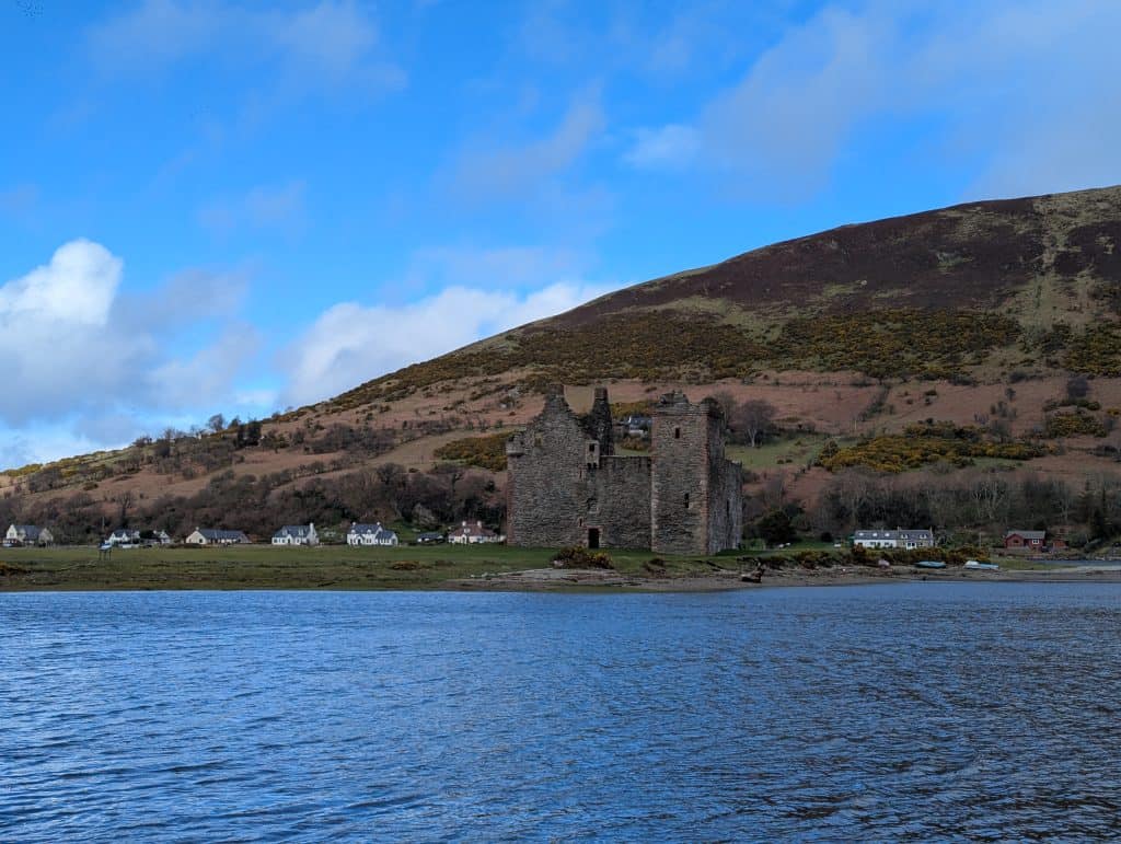 Lochranza castle with a lake, mountains and cottages.